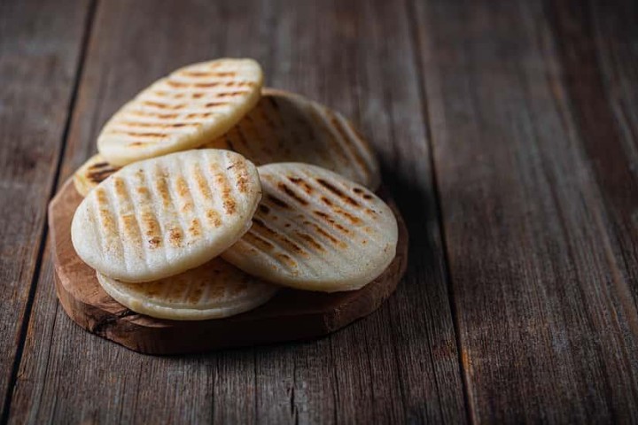 Stack of grilled arepas on a wooden surface.
