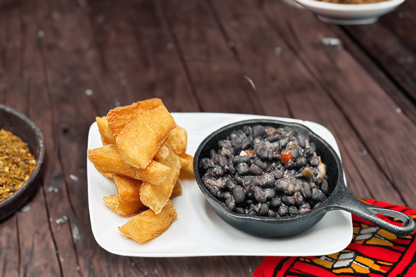 Fried yuca with black beans and vegetable garnish on a wooden surface.