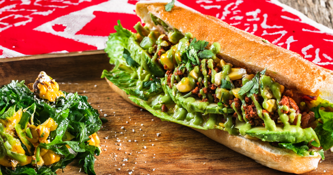Chorizo Avocado Sanguche on a wooden board with vegetables on the side