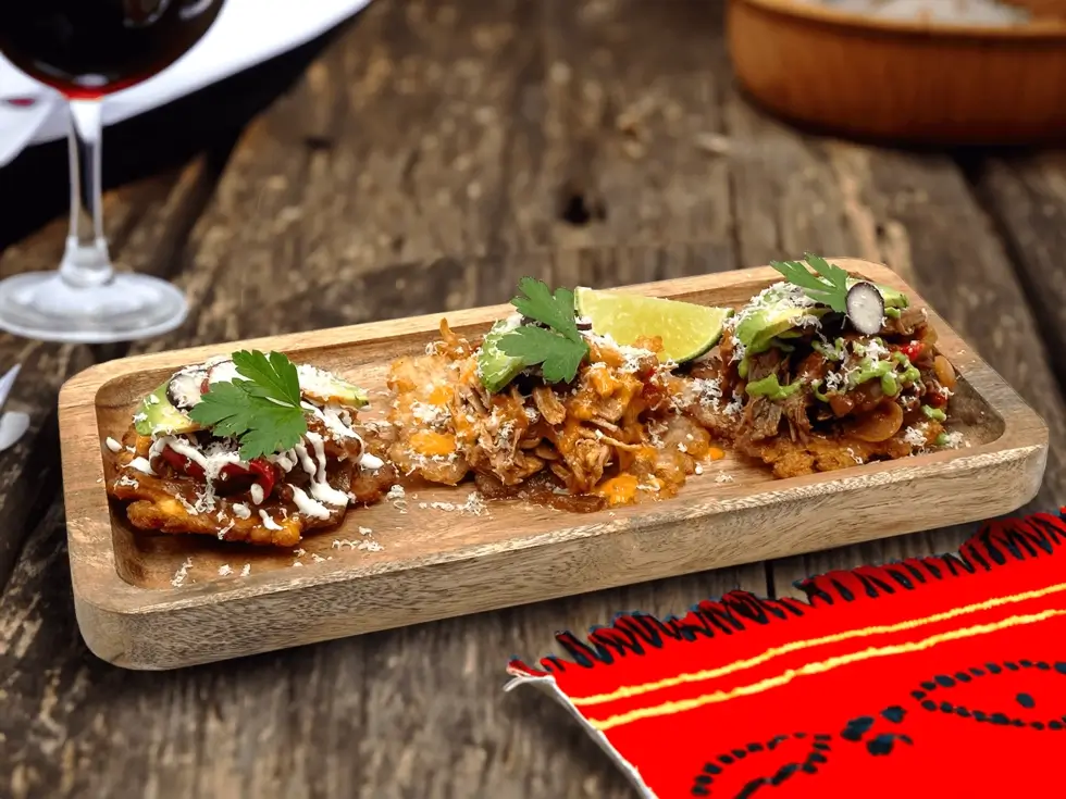 A rustic wooden tray featuring three delicious foods, prominently showcasing golden tostones alongside colorful accompaniments.